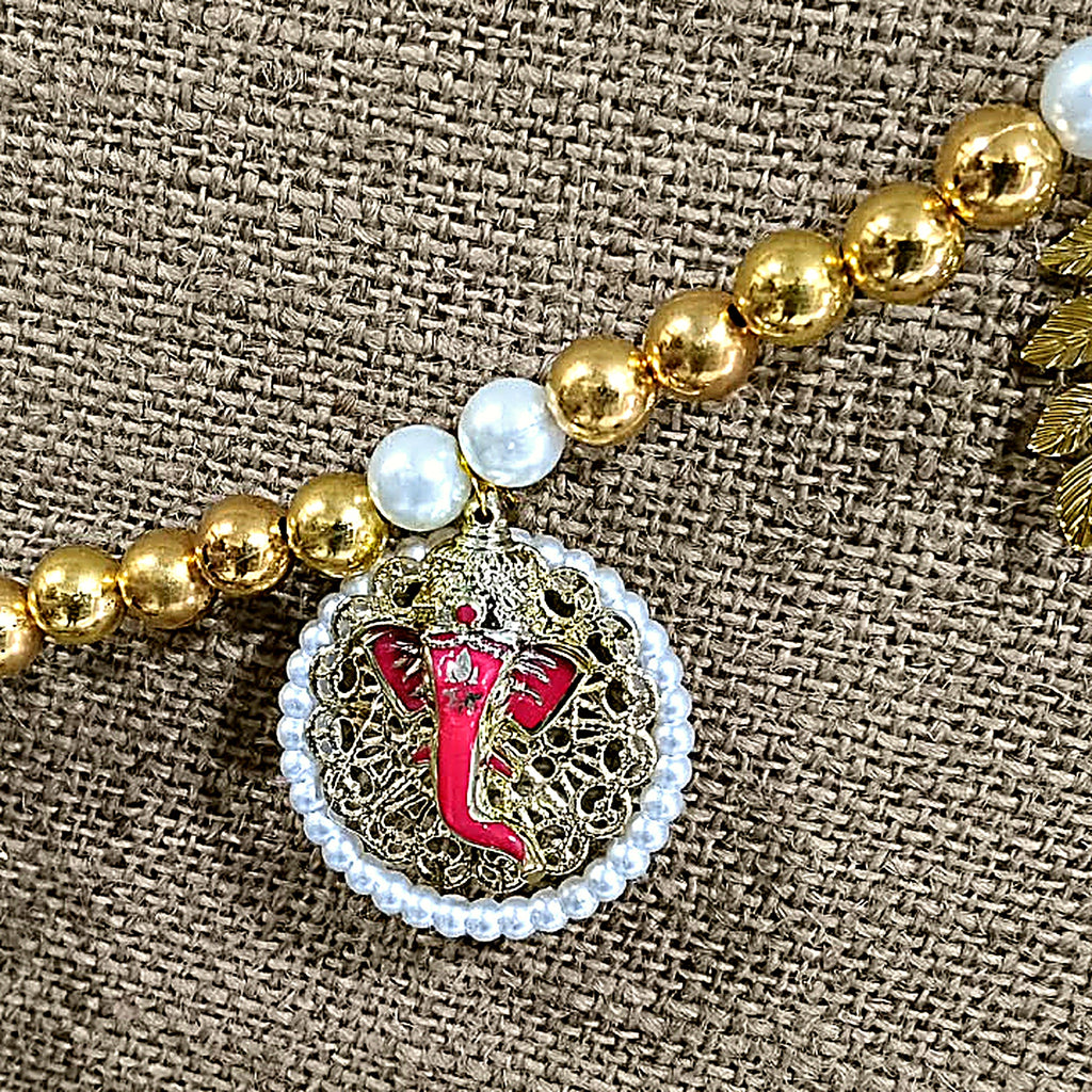 Close-up of pink enamel Ganesha medallion with golden filigree and pearl frame