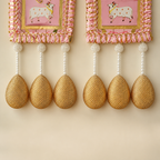 Close-up of pearl strands and textured golden teardrop ornaments on the pink Shubh Labh hangings