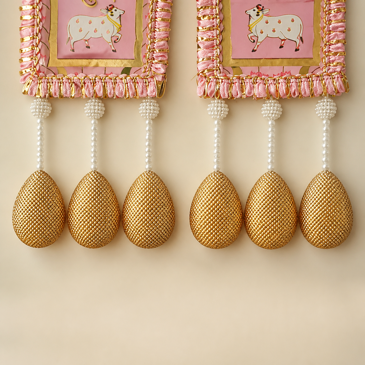 Close-up of pearl strands and textured golden teardrop ornaments on the pink Shubh Labh hangings