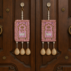 Pink Shubh Labh hanging pair displayed on a carved wooden entrance door